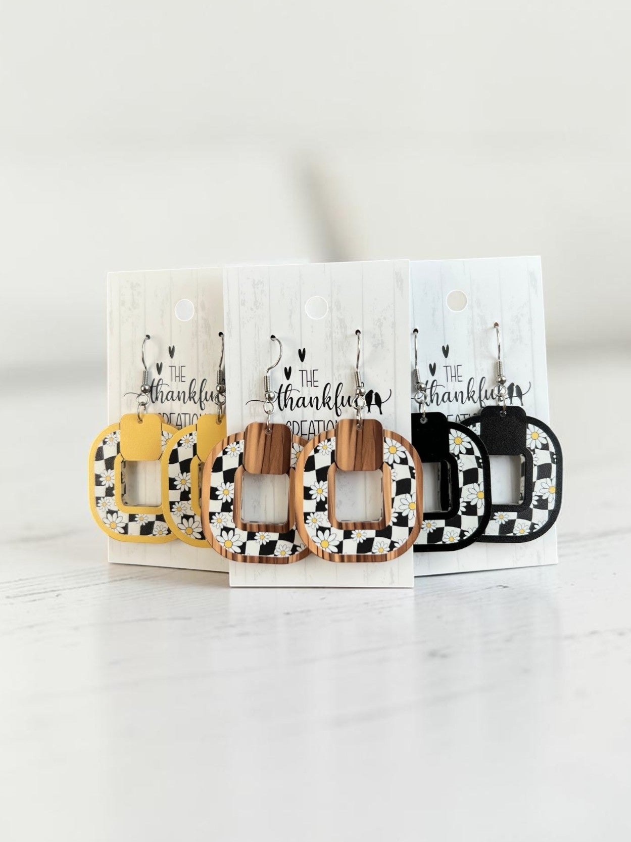 Handmade checkered daisy earrings in yellow, black, and faux wood frames on display cards