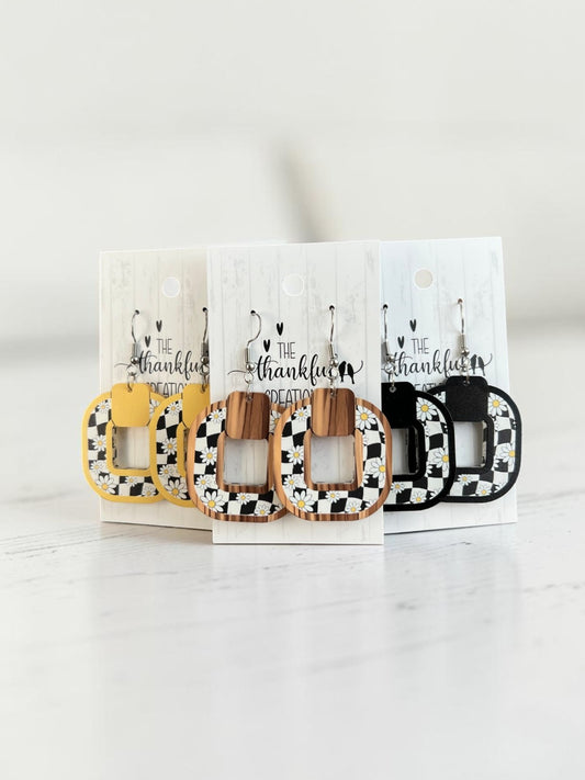 Handmade checkered daisy earrings in yellow, black, and faux wood frames on display cards