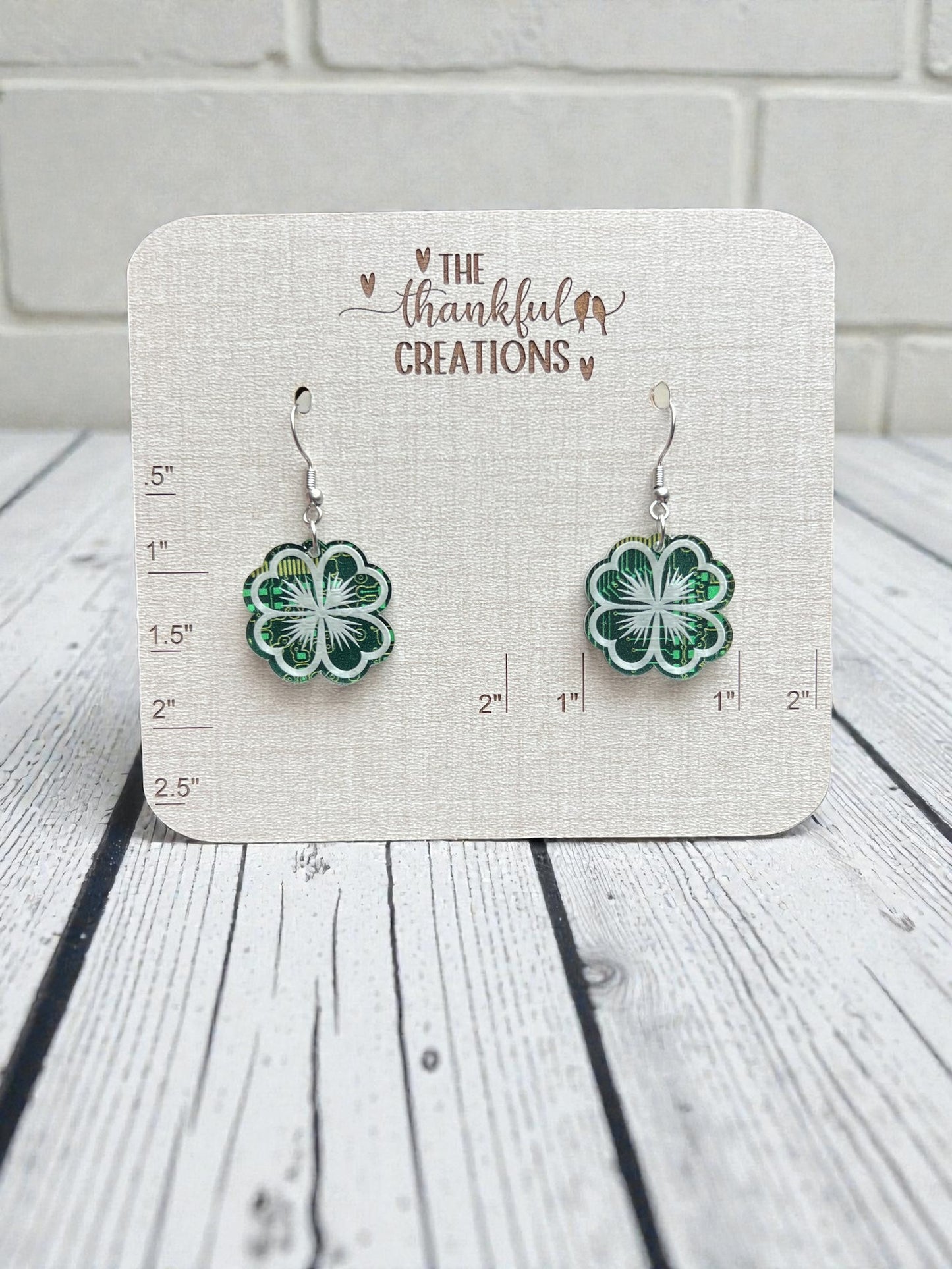Pair of green flower-shaped earrings on a Thankful Creations card against a wooden background