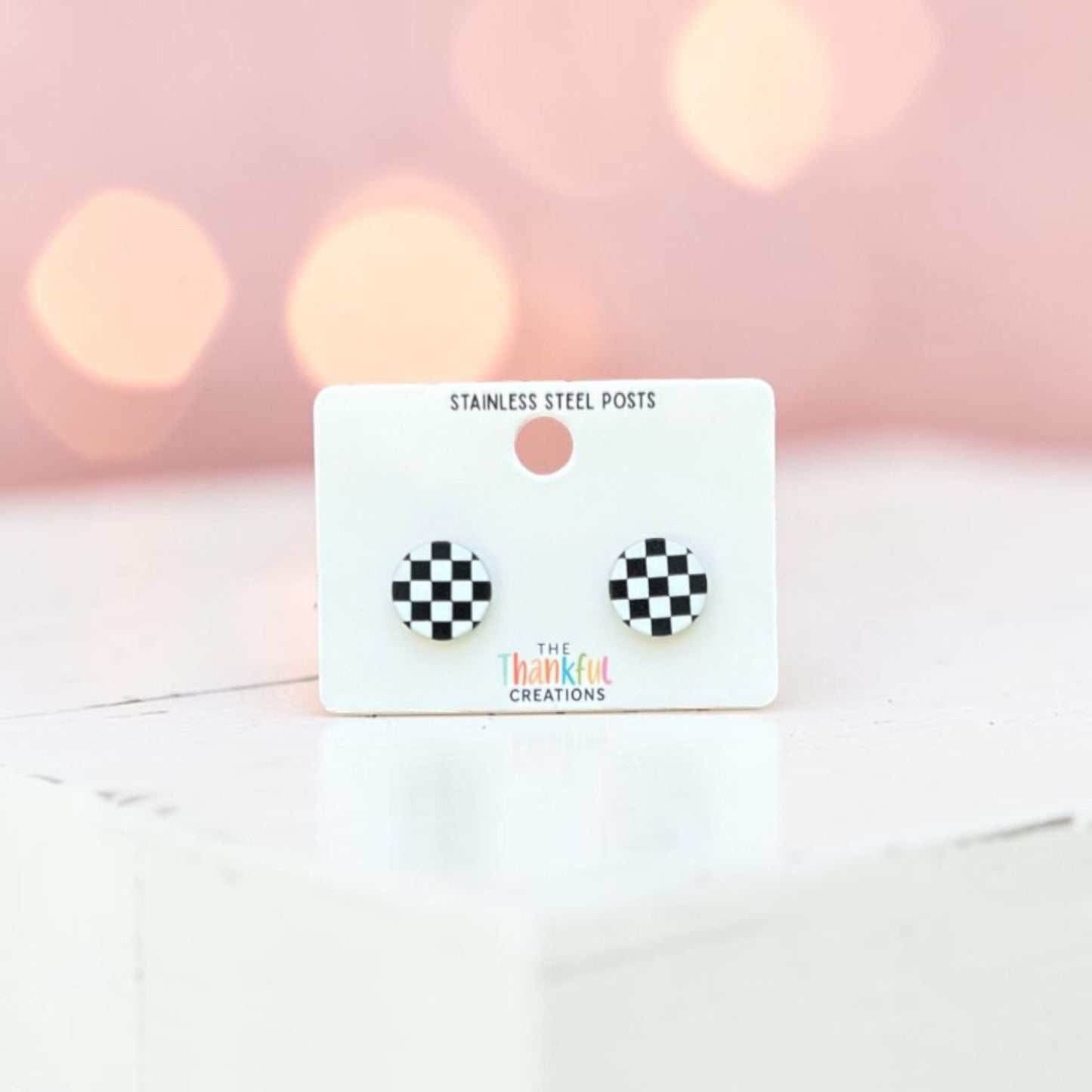 Checkered earrings on a card with a soft pink background