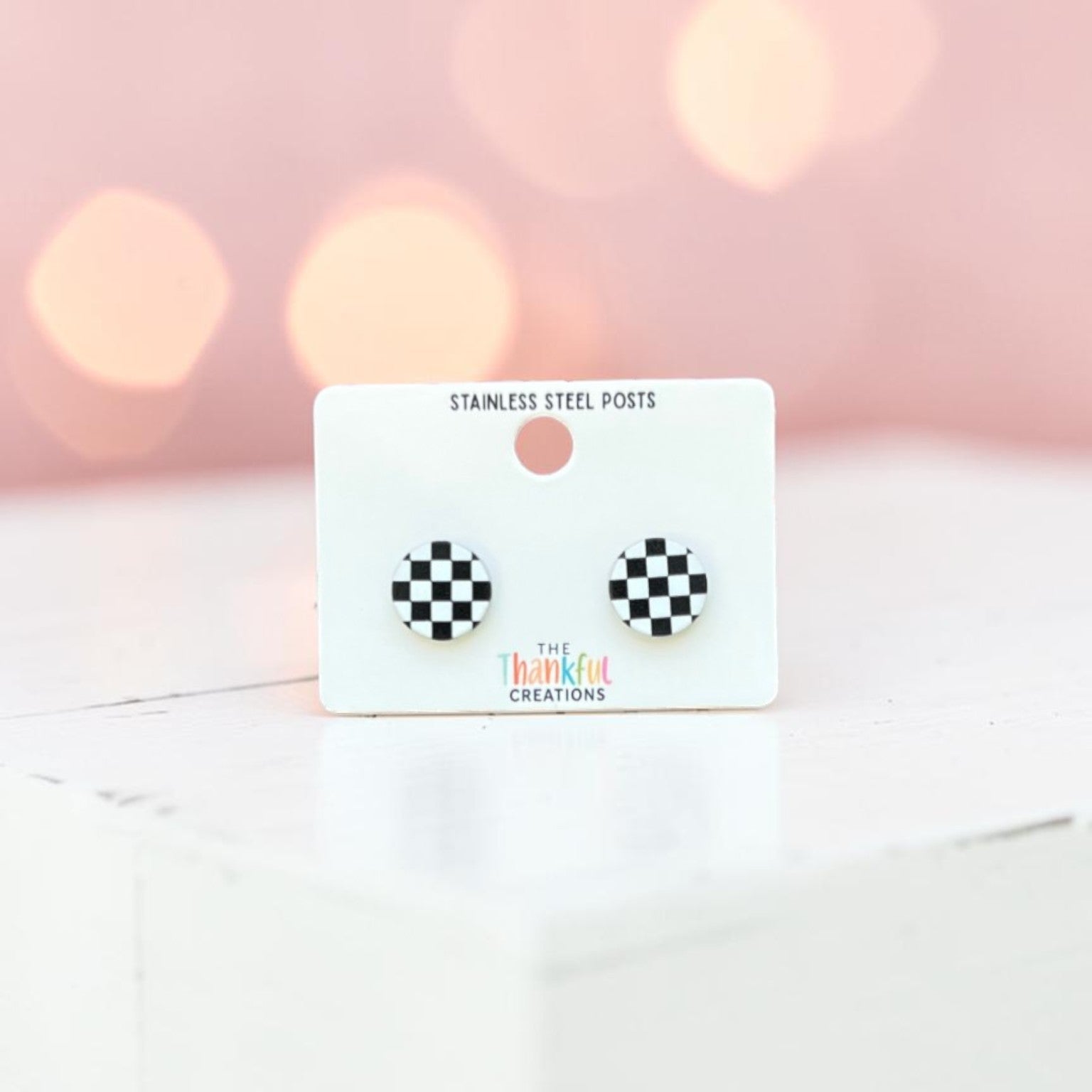 Checkered earrings on a card with a soft pink background